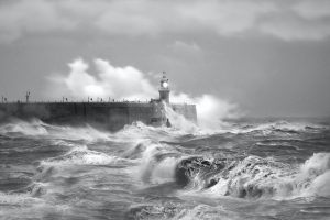 grayscale photo of sea waves crashing on concrete wall