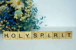 a wooden block spelling the word holy spirit next to a bouquet of flowers